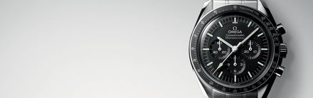 Omega watch with black face and silver case on a light gray background