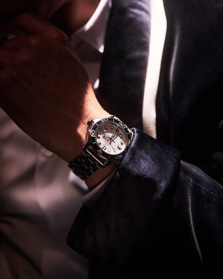 A person in a suit adjusts their collar, wearing a silver luxury wristwatch with a black bezel.