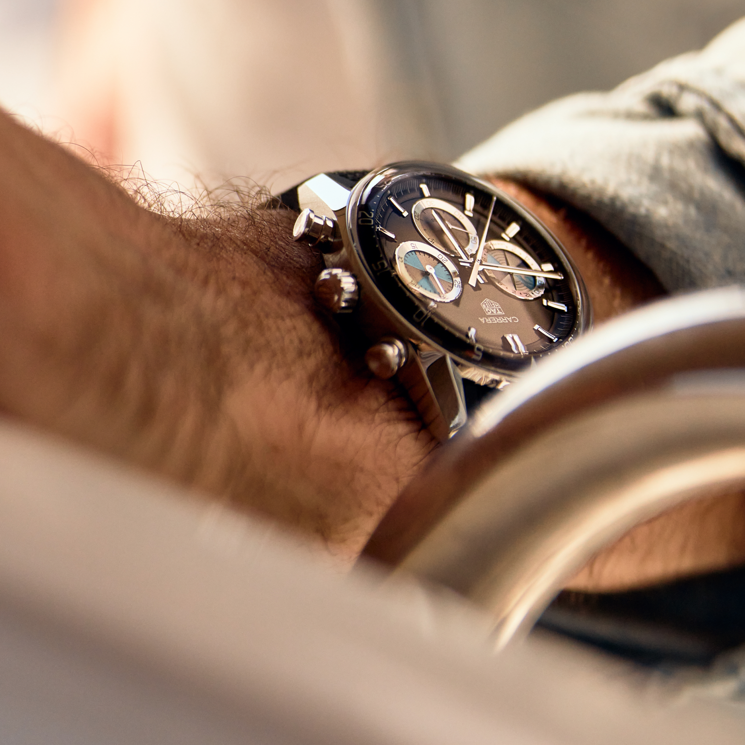 Close-up of a persons wrist wearing the TAG Heuer Carrera Chronograph Seafarer × Hodinkee, a black watch by TAG Heuer featuring silver details and a leather strap.