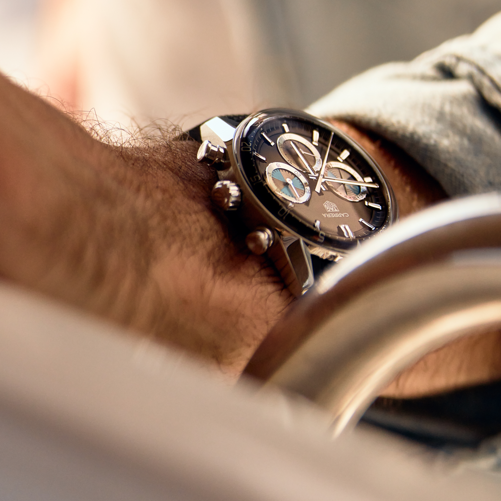 Close-up of a persons wrist wearing the TAG Heuer Carrera Chronograph Seafarer × Hodinkee, a black watch by TAG Heuer featuring silver details and a leather strap.