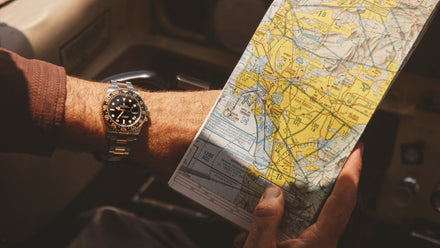 A person holding a yellow navigation map, wearing a black and gold wristwatch.