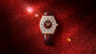 Luxury watch with burgundy dial, diamond-set bezel, gold-tone case, and burgundy leather strap on red glitter background.