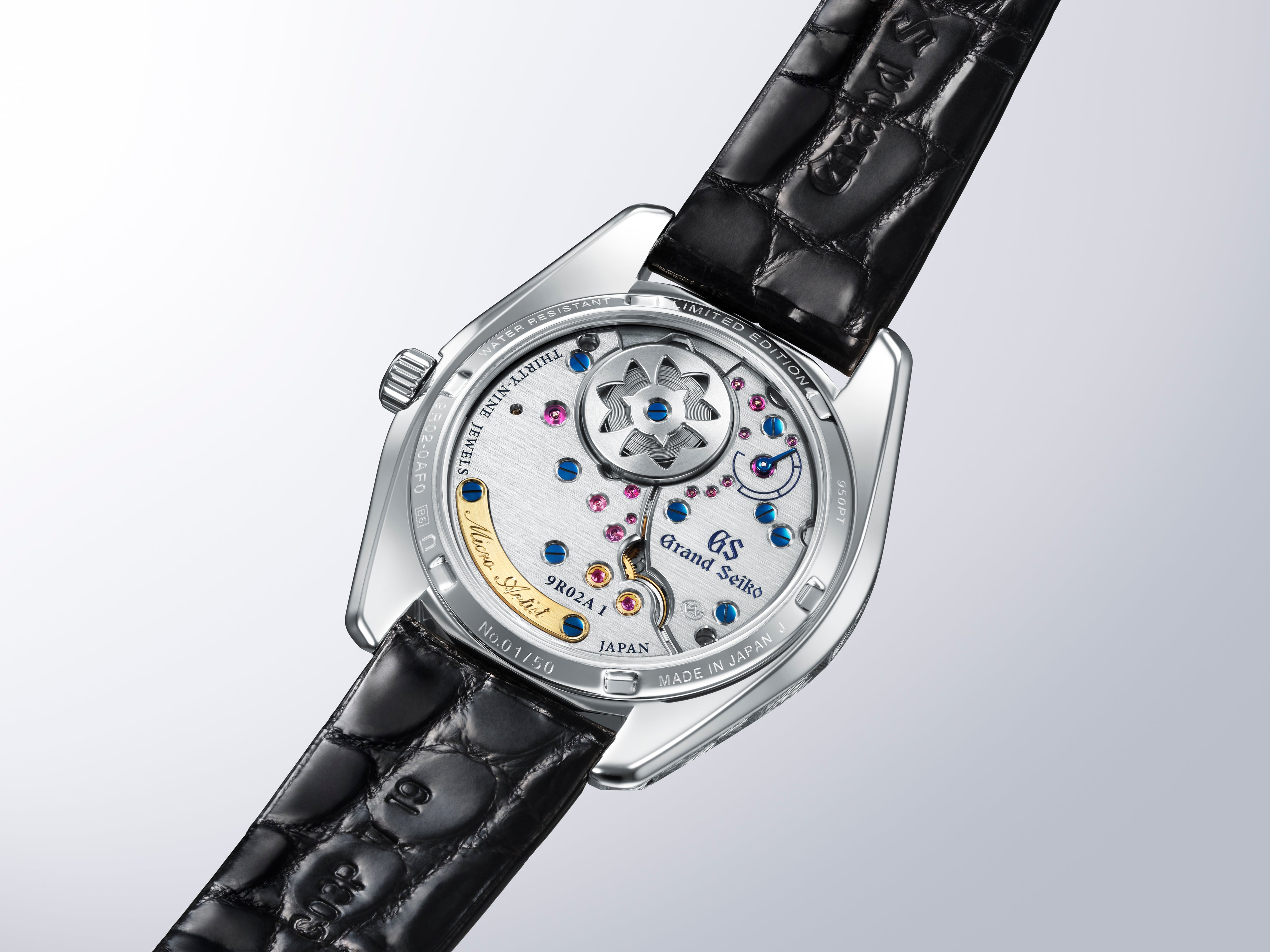 Grand Seiko 44GS watch with silver case, white dial, colorful jeweled movement visible through caseback, and black crocodile 