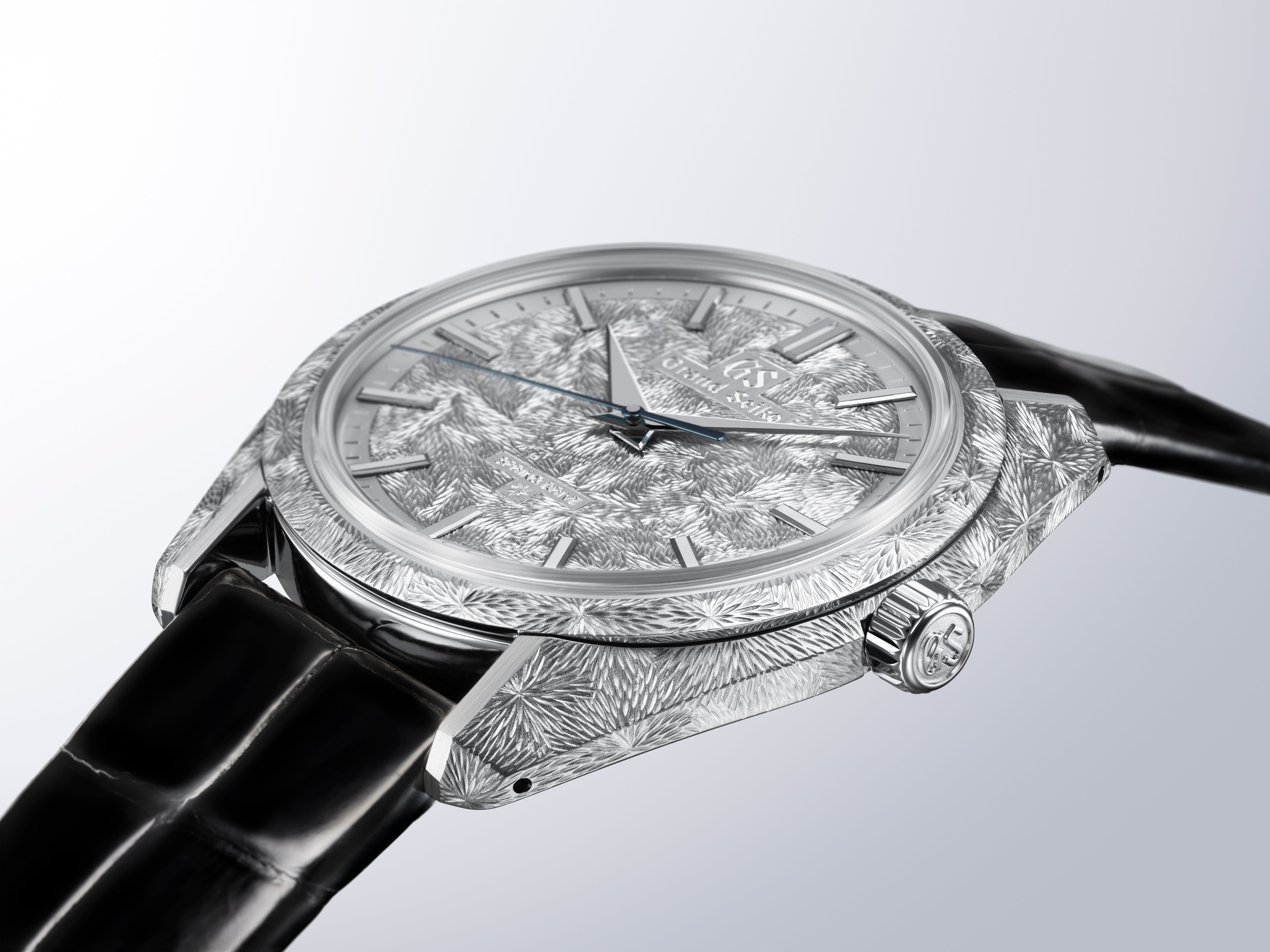 Silver-tone watch with textured dial and case, black leather strap, displayed at an angle against a light background.