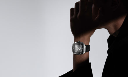 A person in shadow wearing a large, modern wristwatch, with their hand near their face.