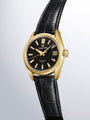 Gold-tone Grand Seiko watch with black dial, gold hour markers, date window, and black crocodile leather strap.
