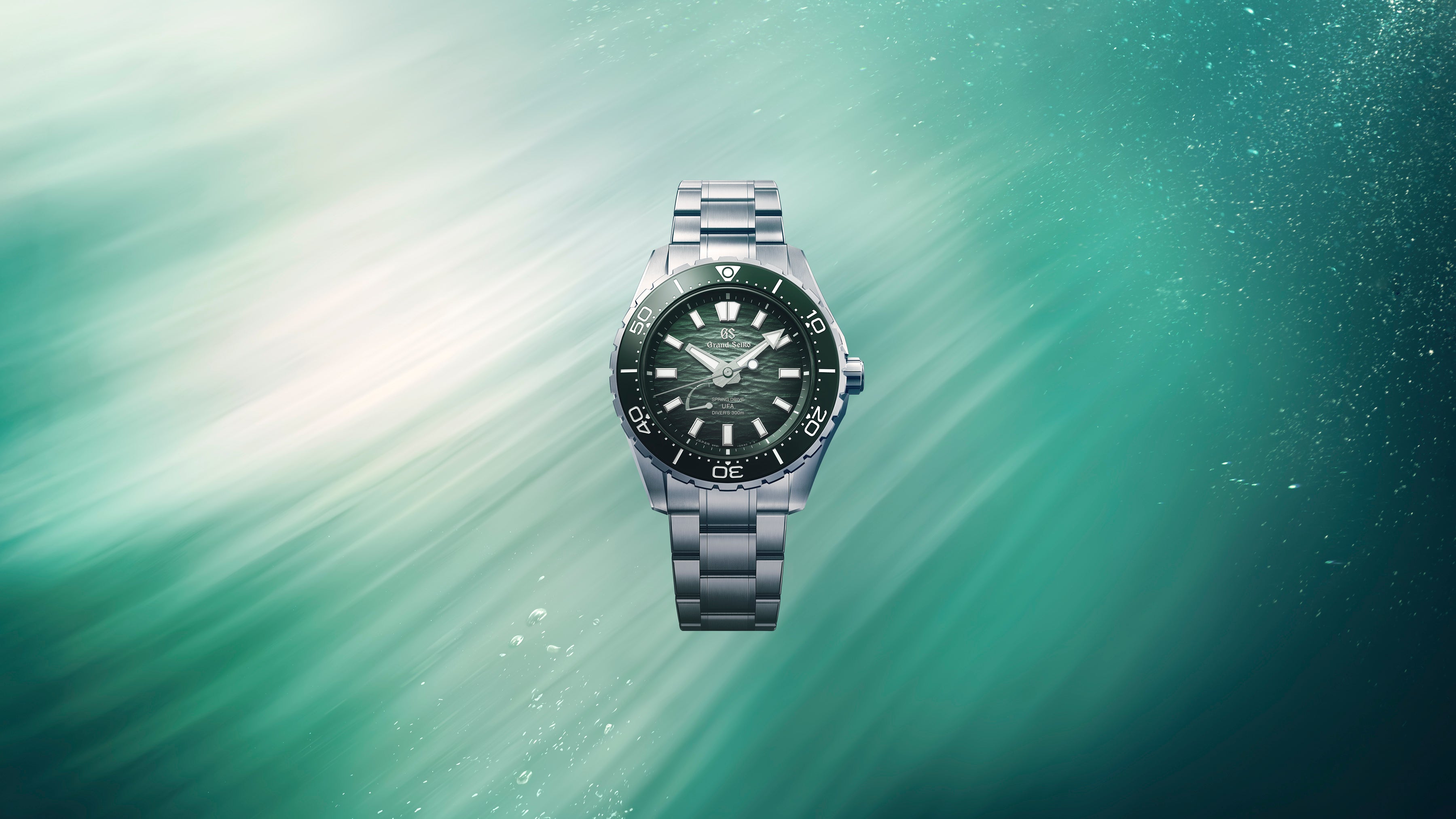 Steel diver watch with black dial, luminous hour markers, rotating bezel, and matching steel bracelet against teal water back