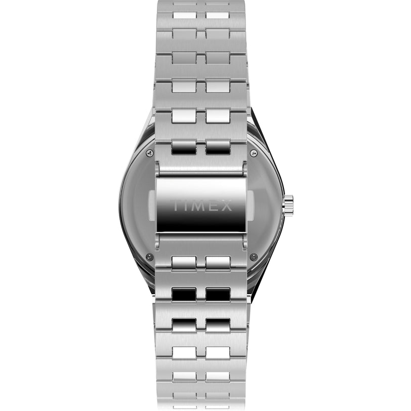A silver Q Timex GMT by Timex is shown from the back, highlighting its brushed metal bracelet and clasp. “TIMEX” is engraved on the case back, and the crown appears on the right side.