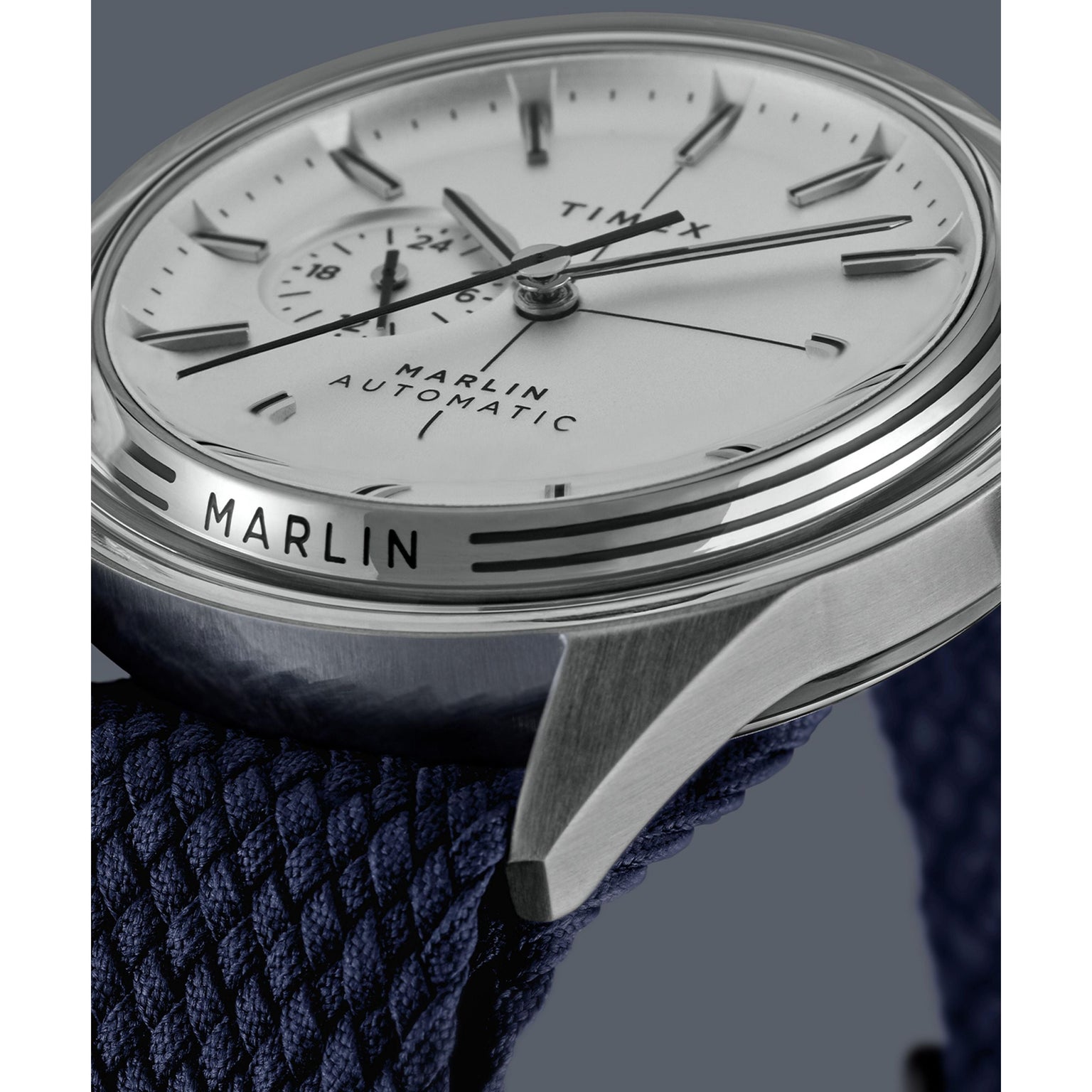 Close-up of a Timex Marlin® Jet Automatic wristwatch, showcasing a domed Hesalite crystal over a white dial with black hour markers and a blue textured strap. The words MARLIN® JET AUTOMATIC and TIMEX are visible on its retro-futuristic design.
