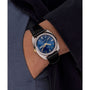 A person in a dark jacket and blue shirt wears the Timex G SS QZ SW 1978 DAY DTE 37.5 BLU DL 25, a retro dress watch with blue sunray dial, silver case, gold crown, black leather strap, and day-date display.