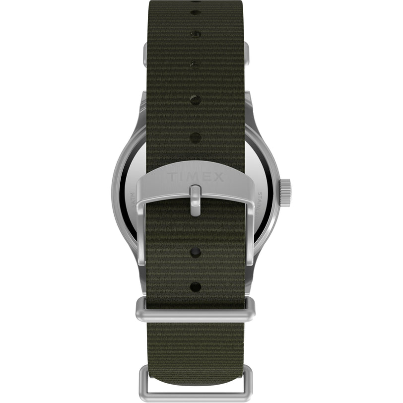 A close-up of the Timex G SS MW SW MK1 36 BLK DL GRN STP 25 shows its military-style back, dark green recycled fabric strap, and silver buckle engraved with the Timex brand name.