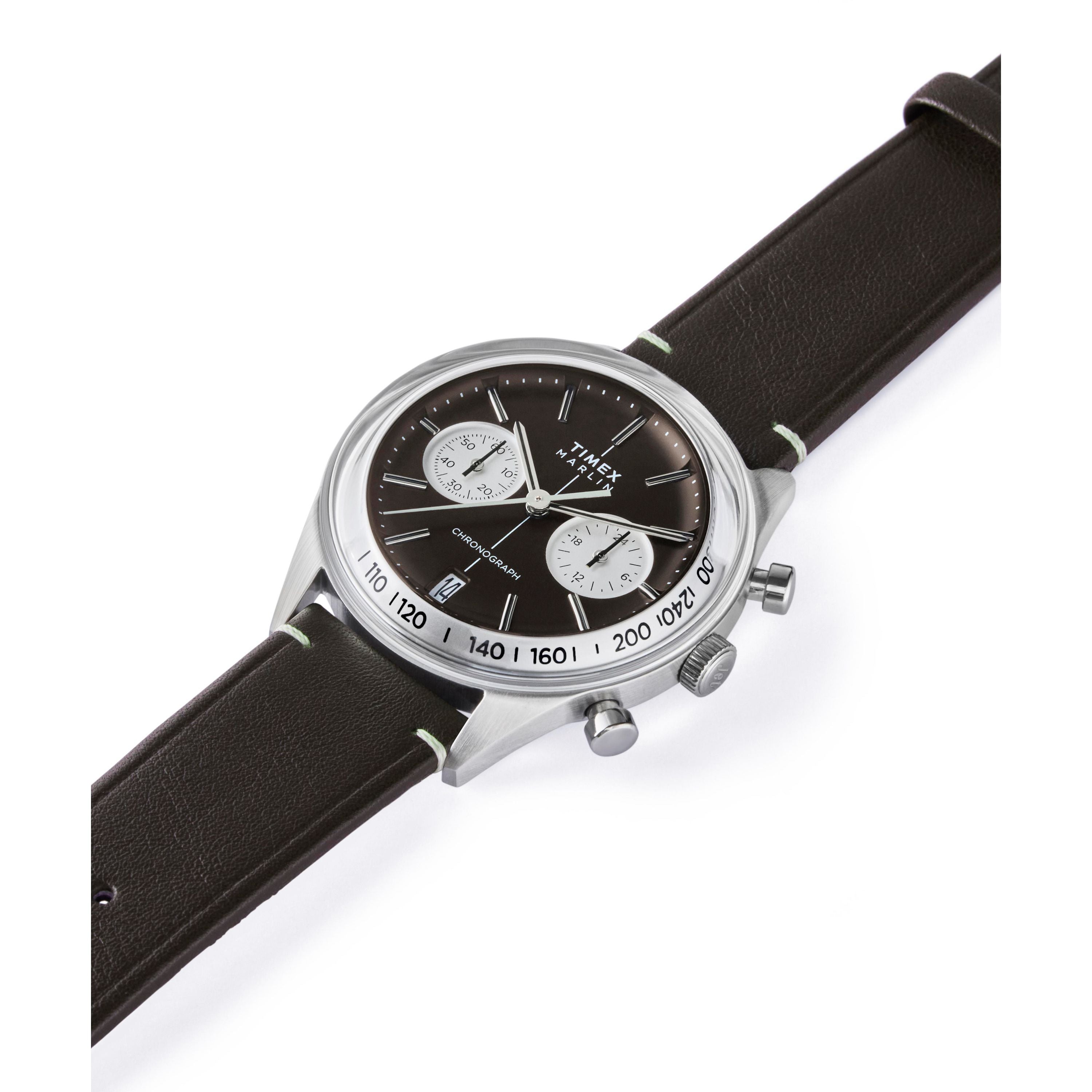 A Timex G SS QZ SW JET 40 BROWN DL BWN STP 25 watch with a silver case, black face, domed Hesalite crystal, two white subdials, chronograph and date display, and a dark brown leather strap is shown angled on a white background.