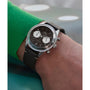 A person wearing a green sleeve shows off a Timex G SS QZ SW JET 40 BROWN DL BWN STP 25 with a domed crystal, black dial, white subdials, and brown leather strap on their left wrist.