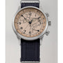 The Timex Waterbury Traditional Fly-Back Chronograph features a stainless steel case, beige dial with black numerals, fly-back chronograph subdials, date window, and a textured dark navy fabric strap.