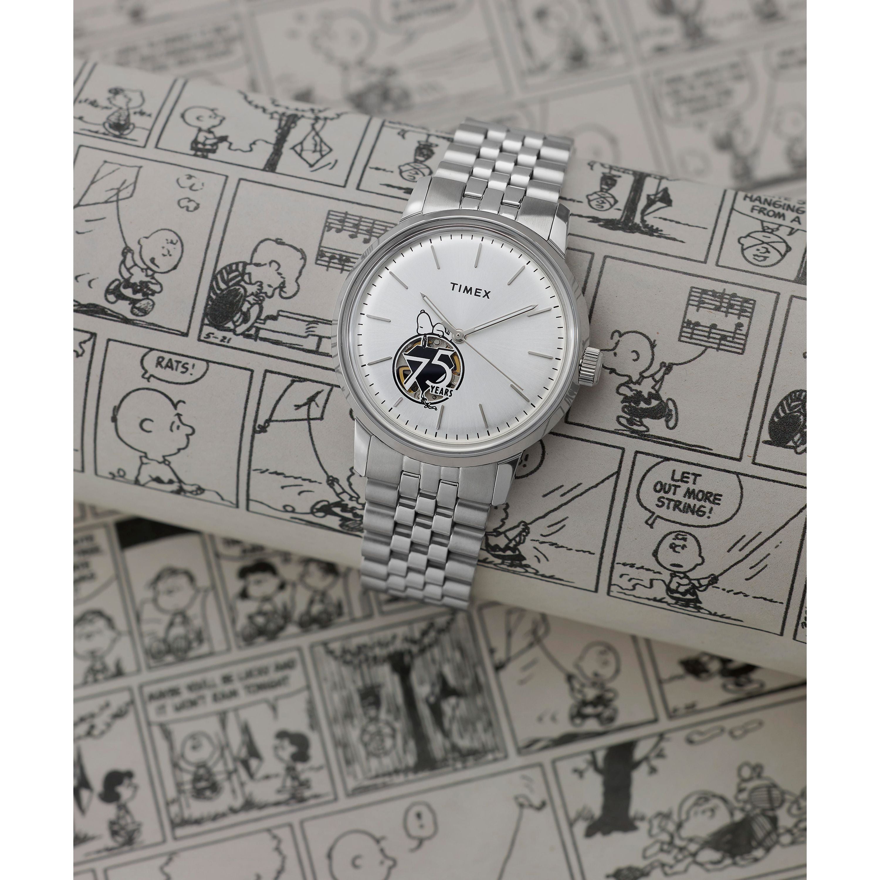 The Timex G SS AU BW PEANUTS MARLIN 75 ANNI EDI 25 watch, honoring Peanuts' 75th anniversary, features a silver case and a Snoopy illustration on the dial, displayed atop black-and-white Peanuts comic strips.