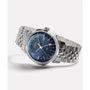 The Timex Marlin® Quartz GMT, featuring a stainless steel case, blue dial, date window, silver markers, and red-tipped GMT hand on a metal bracelet, is shown at an angle against a plain white background.