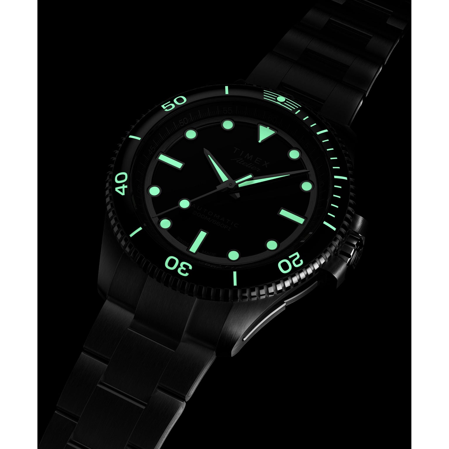 The Timex Atelier Marine M1a Swiss Made Automatic, a black metal wristwatch with luminous green hour markers and hands, glows in the dark. Its minimalist design stands out against a black background, showcasing its modern features.