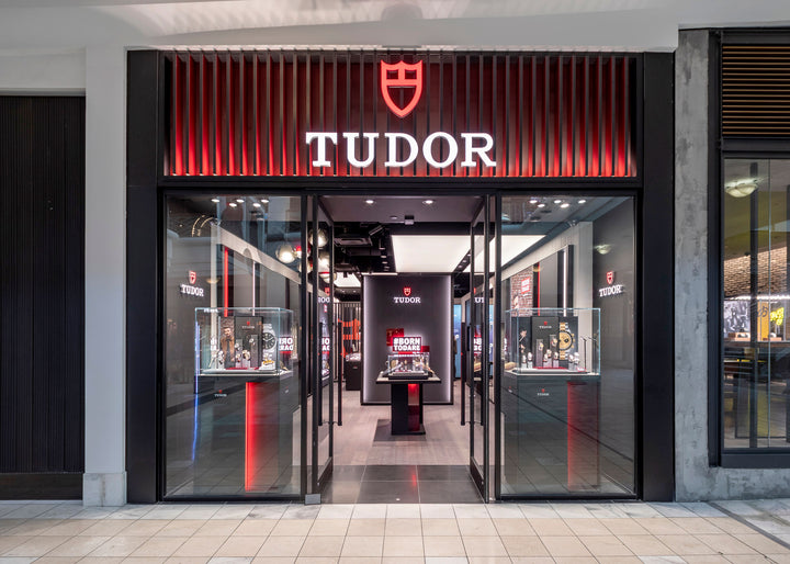 TUDOR watch store with illuminated sign, glass display cases, and modern interior in a shopping mall.