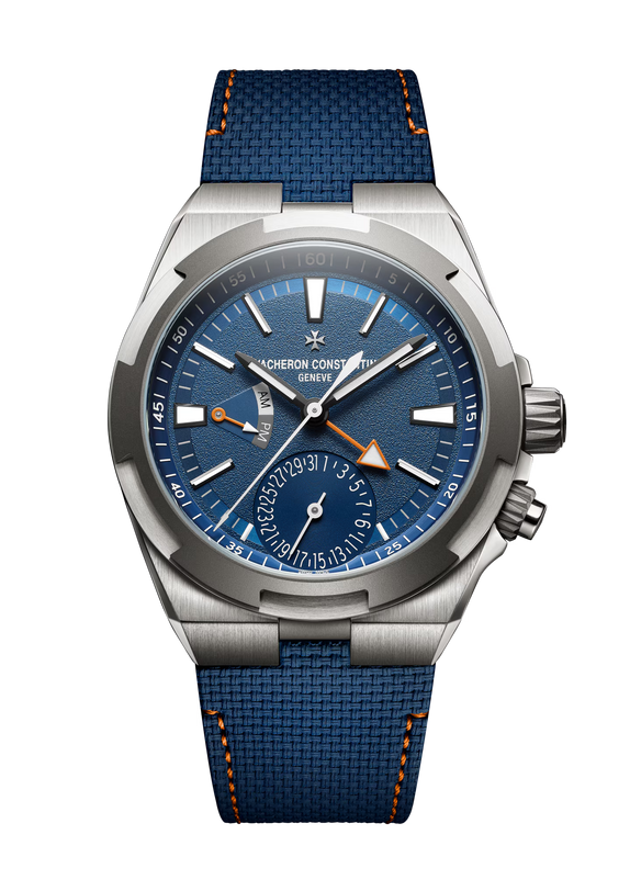 Stainless steel watch with blue dial, dual time zone display, orange accents, and blue textile strap with orange stitching.