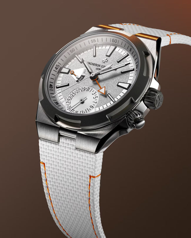 Vacheron Constantin watch with silver dial, dual time zone subdial, white fabric strap with orange stitching, and black bezel