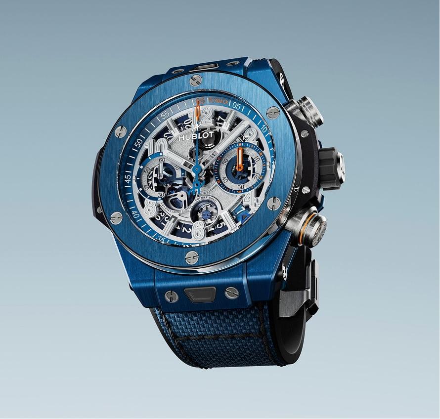 Blue ceramic chronograph watch with skeletal dial, metallic subdials, and dark fabric strap against light background.