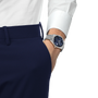 Silver-toned watch with dark blue dial worn on wrist with white shirt cuff and navy pants.