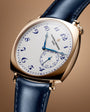 Gold-tone watch with white dial, blue Arabic numerals, blue hands, and dark blue leather strap.