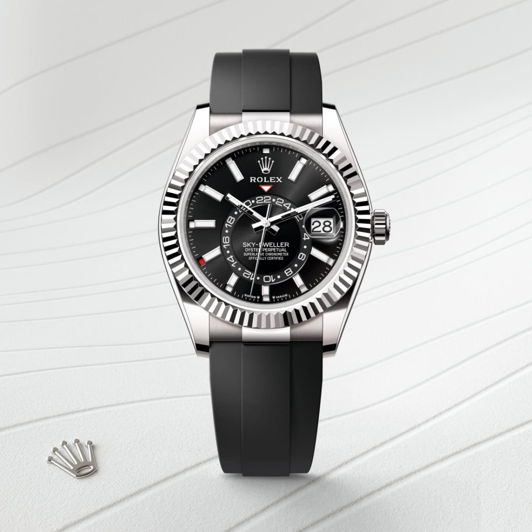 A black Rolex Sky-Dweller watch with a rubber strap is displayed on a light, textured surface.