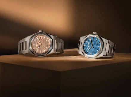 Two watches on a wooden surface with a warm light source.