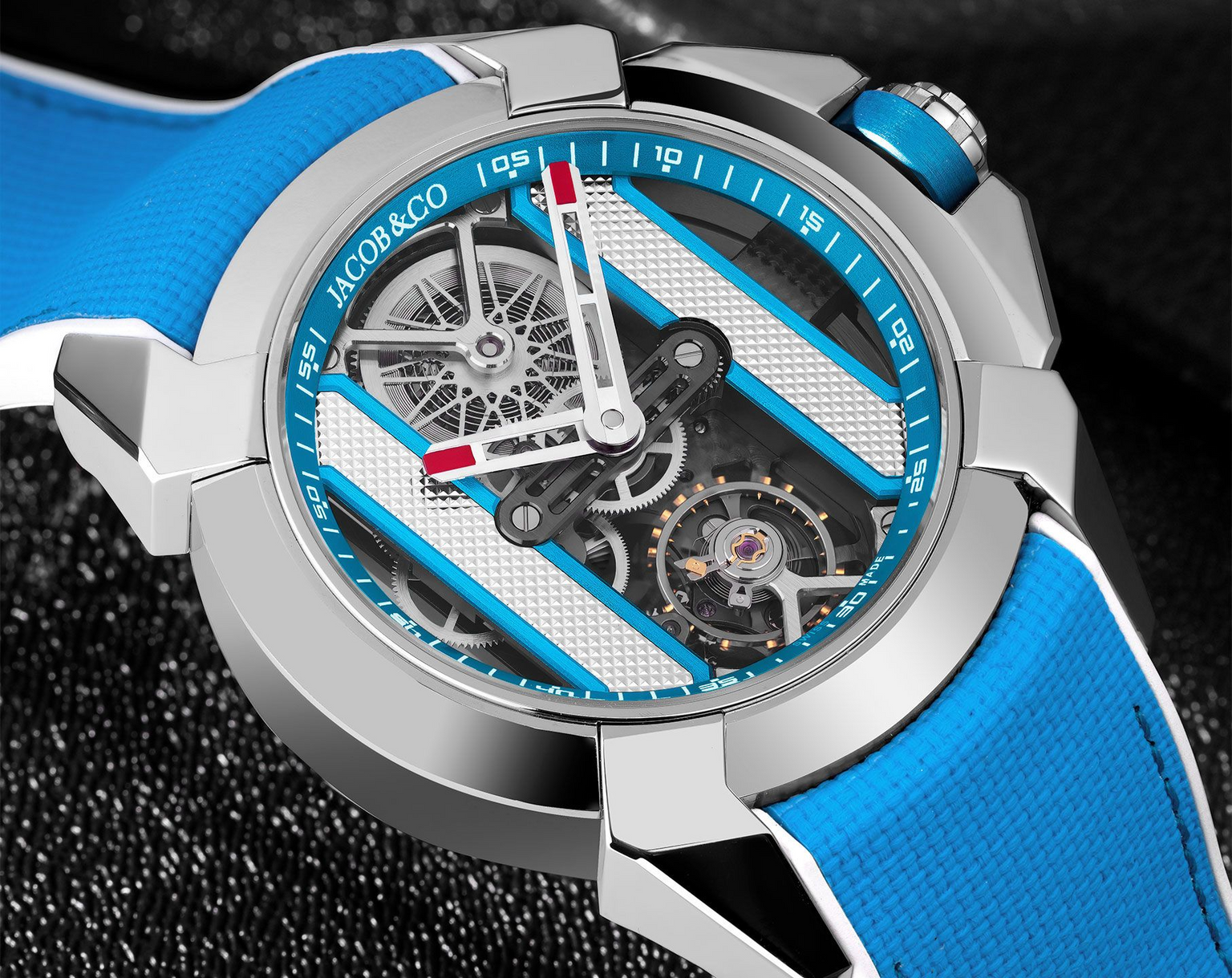 Stainless steel watch with blue and white dial, exposed skeletal movement, red hands, and blue rubber strap.