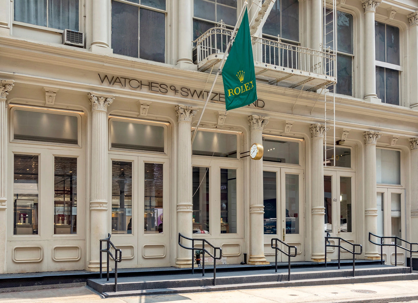 Rolex flag outside a Watches of Switzerland store with tall columns and large windows.