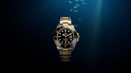A gold and silver luxury dive watch underwater with bubbles rising to the surface.