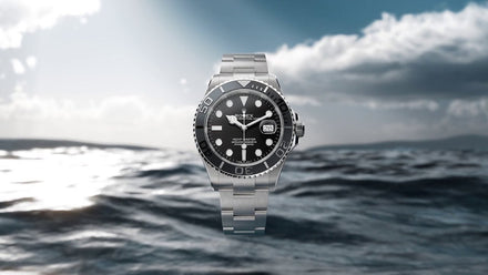 A silver and black wristwatch floats above the ocean with a cloudy sky in the background.