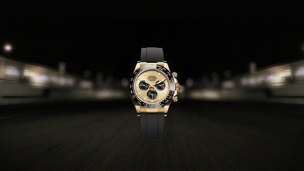 Gold luxury wristwatch with black strap displayed against a blurred, dark background with lights.