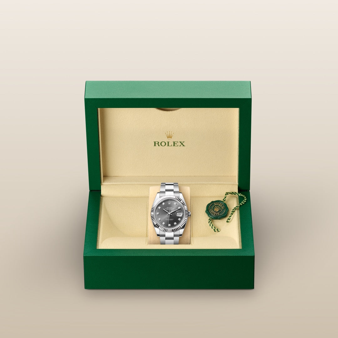 A silver Rolex watch in a green and beige box, with a green tag beside it.