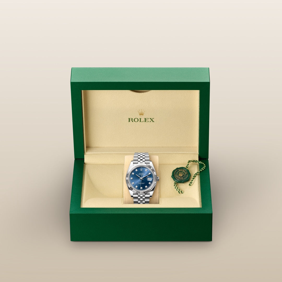 A Rolex watch with a blue face in an open green and beige box with a green tag beside it.