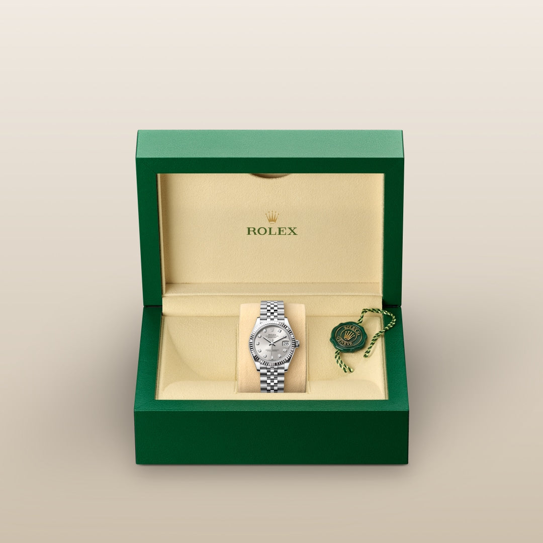 A silver Rolex watch in a green and beige presentation box with branding and a tag beside it.