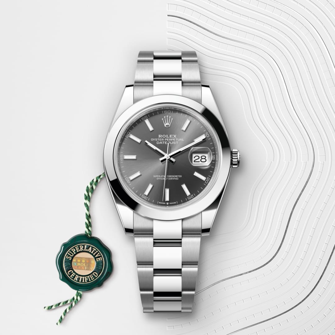 A silver Rolex Datejust watch with a grey dial and date display, next to a green Superlative Certified tag.