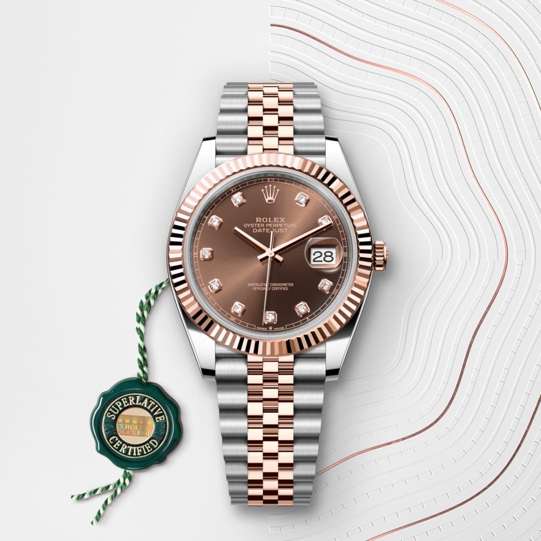 A Rolex watch with a two-tone metal band, diamond hour markers, and a date window, beside a green certified tag.