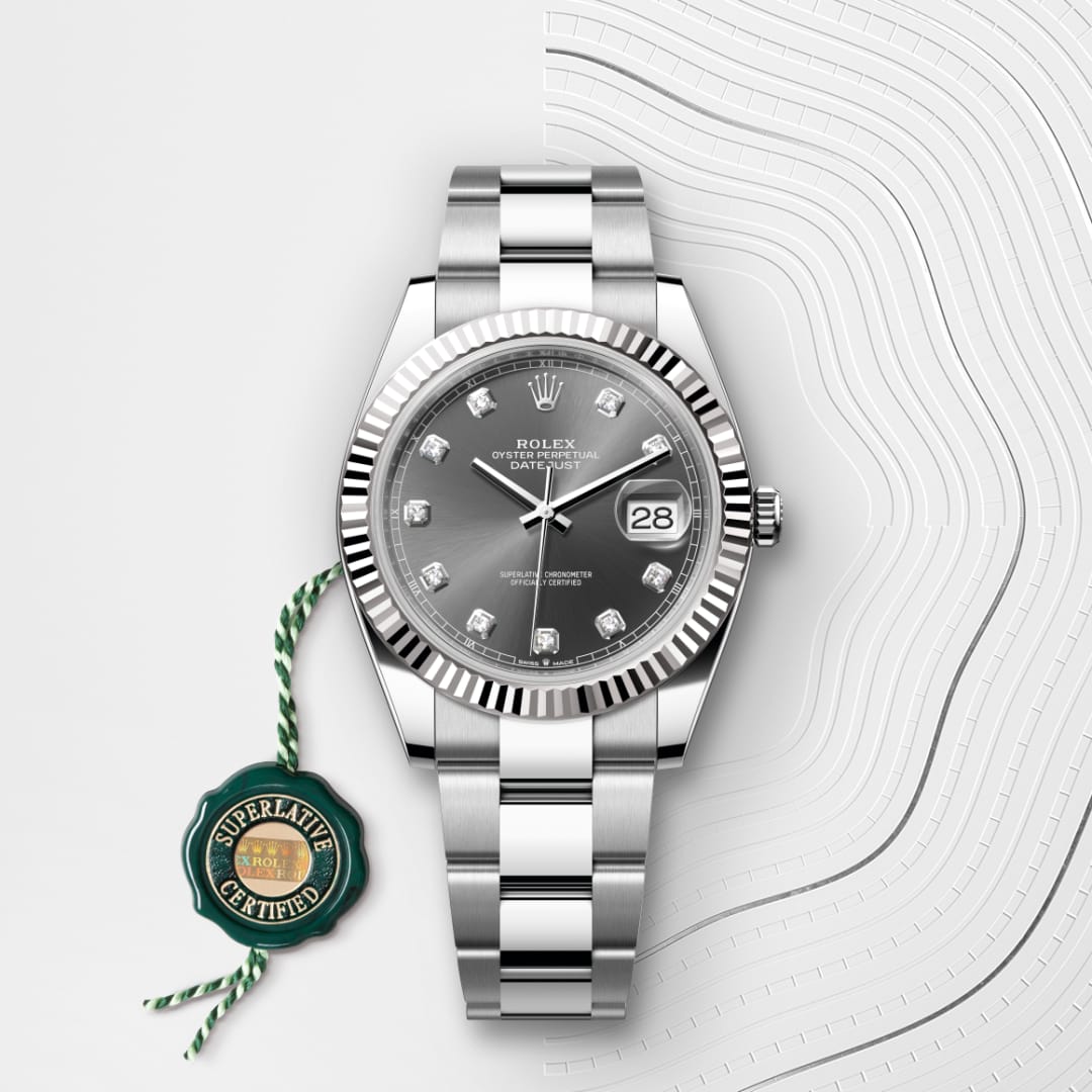 A silver Rolex watch with a dark face and date display, next to a green Superlative Certified tag.
