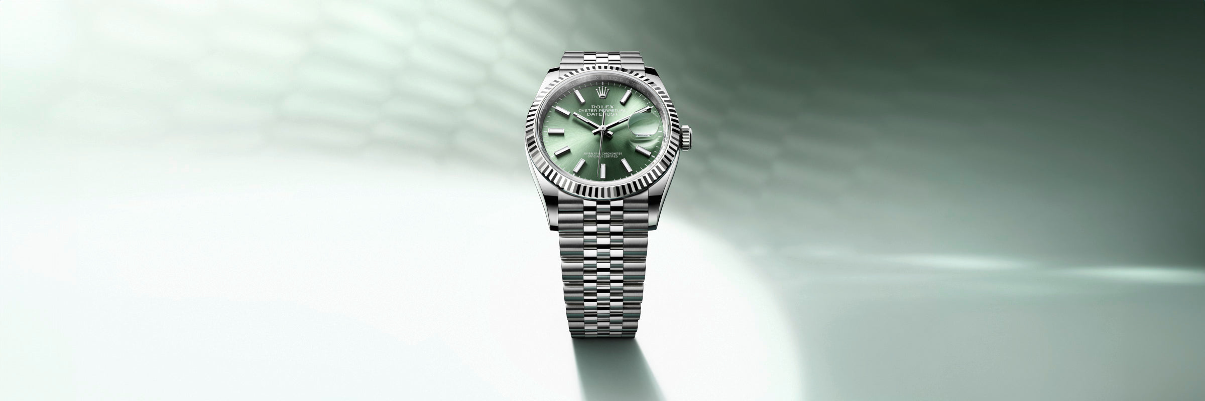 A silver wristwatch with a green dial on a matching metal band, set against a gradient green background.