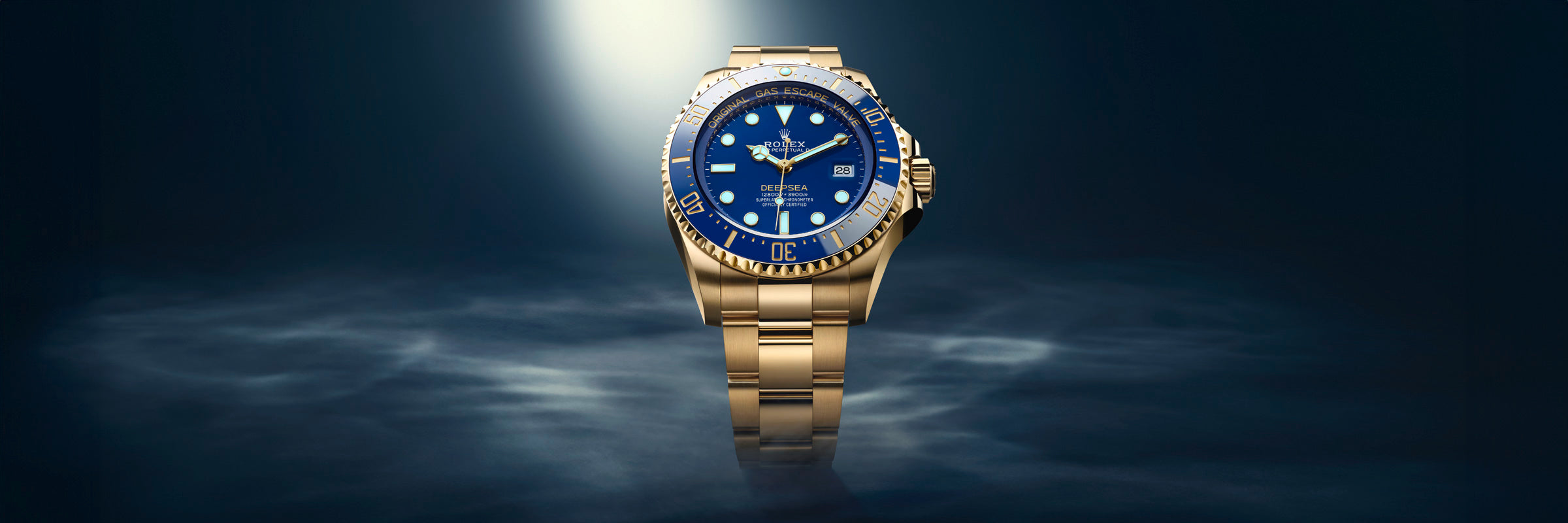 A gold wristwatch with a blue face is spotlighted against a dark, misty background.