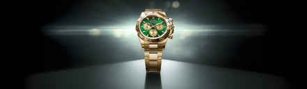 A gold wristwatch with a green dial displayed under dramatic lighting on a dark background.