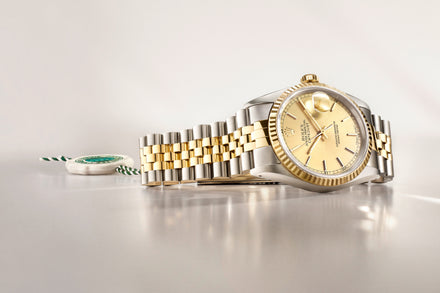 A gold and silver Rolex watch with a champagne dial displayed on a light, reflective surface.