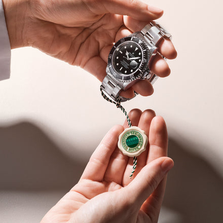 Two hands holding a Rolex submariner watch with the Rolex Certified Pre Owned badge close up