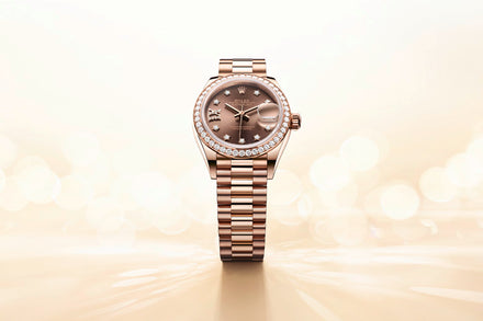 A rose gold luxury wristwatch with diamond bezel and chocolate dial, displayed on a soft, glowing background.