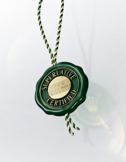 A green wax seal tag with Superlative Certified and Rolex hanging from a green and gold braided string.