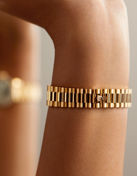 Close-up of a gold watch bracelet featuring the Rolex crown logo on a persons wrist.