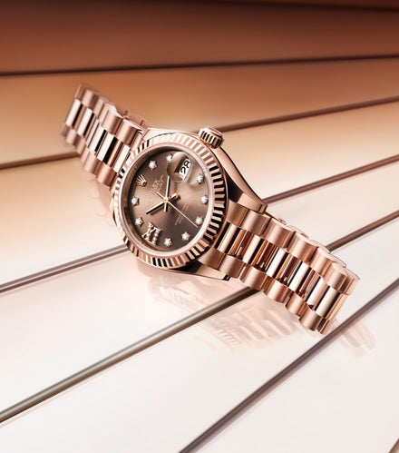 A rose gold wristwatch with a diamond-studded dial displayed on a glossy, striped surface.