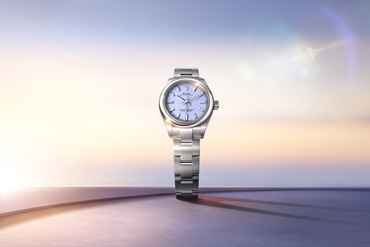 A silver wristwatch with a pale blue face displayed against a soft, pastel-colored gradient background.